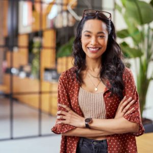 istockphoto-1496613385-612×612 Portrait of smiling young multiethnic woman looking at camera with crossed arms. Successful latin business woman standing in modern office with copy space. Young university hispanic girl with pleasant smile and folded arms.